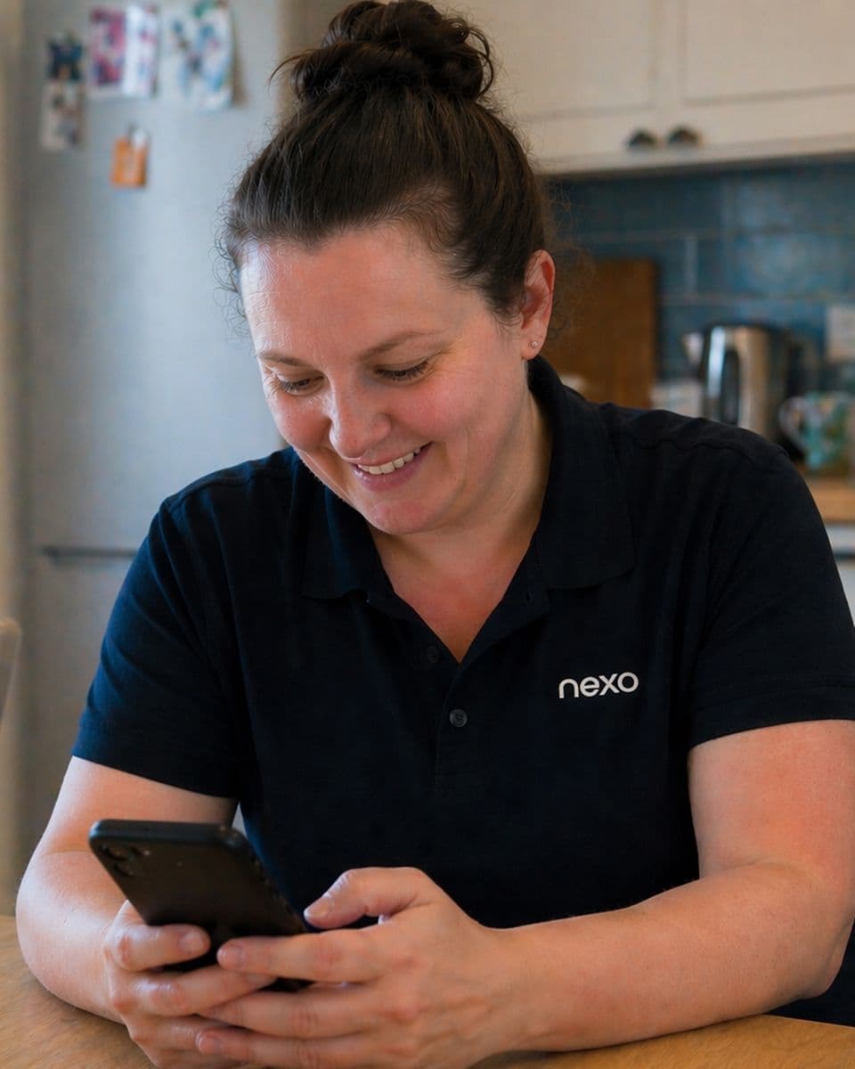 Smiling Nexo care worker in a navy uniform checking her phone in a kitchen